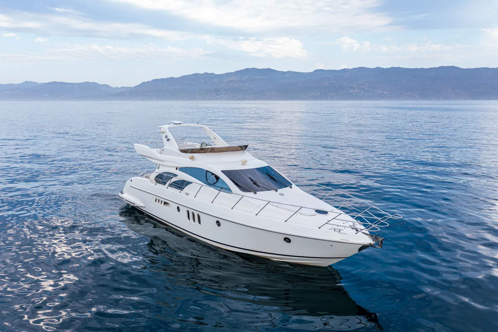 White yacht on calm open ocean with mountains in the distance