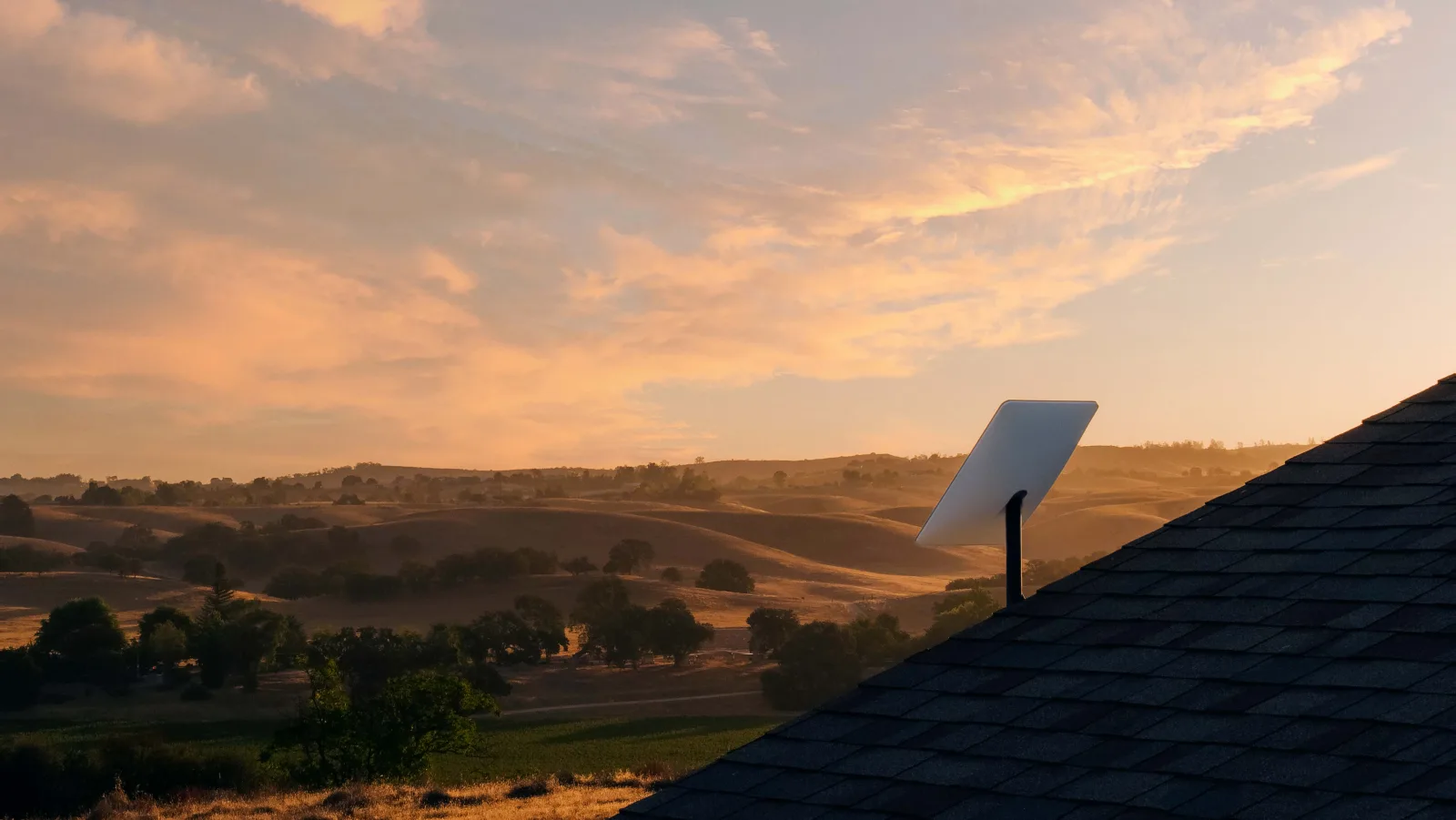 Starlink dish on a rooftop overlooking rural hills at sunset